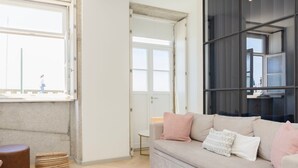 A modern living room with a beige sofa, a wooden floor, and a large window. - Liiiving in Porto - Modern Coastline Apartment (Porto)