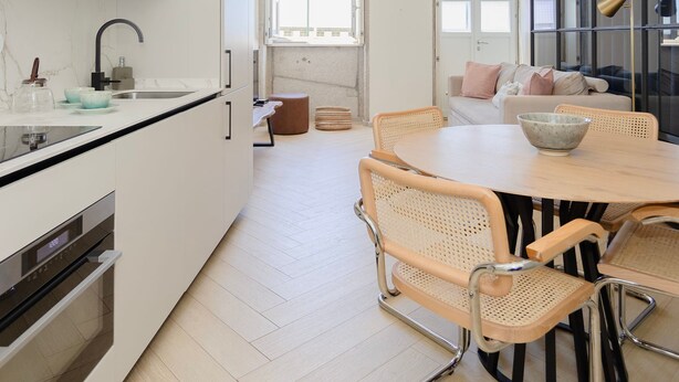A modern kitchen with a dining area, featuring a large window, a built-in oven, and a dining table with chairs. - Liiiving in Porto - Modern Coastline Apartment (Porto)