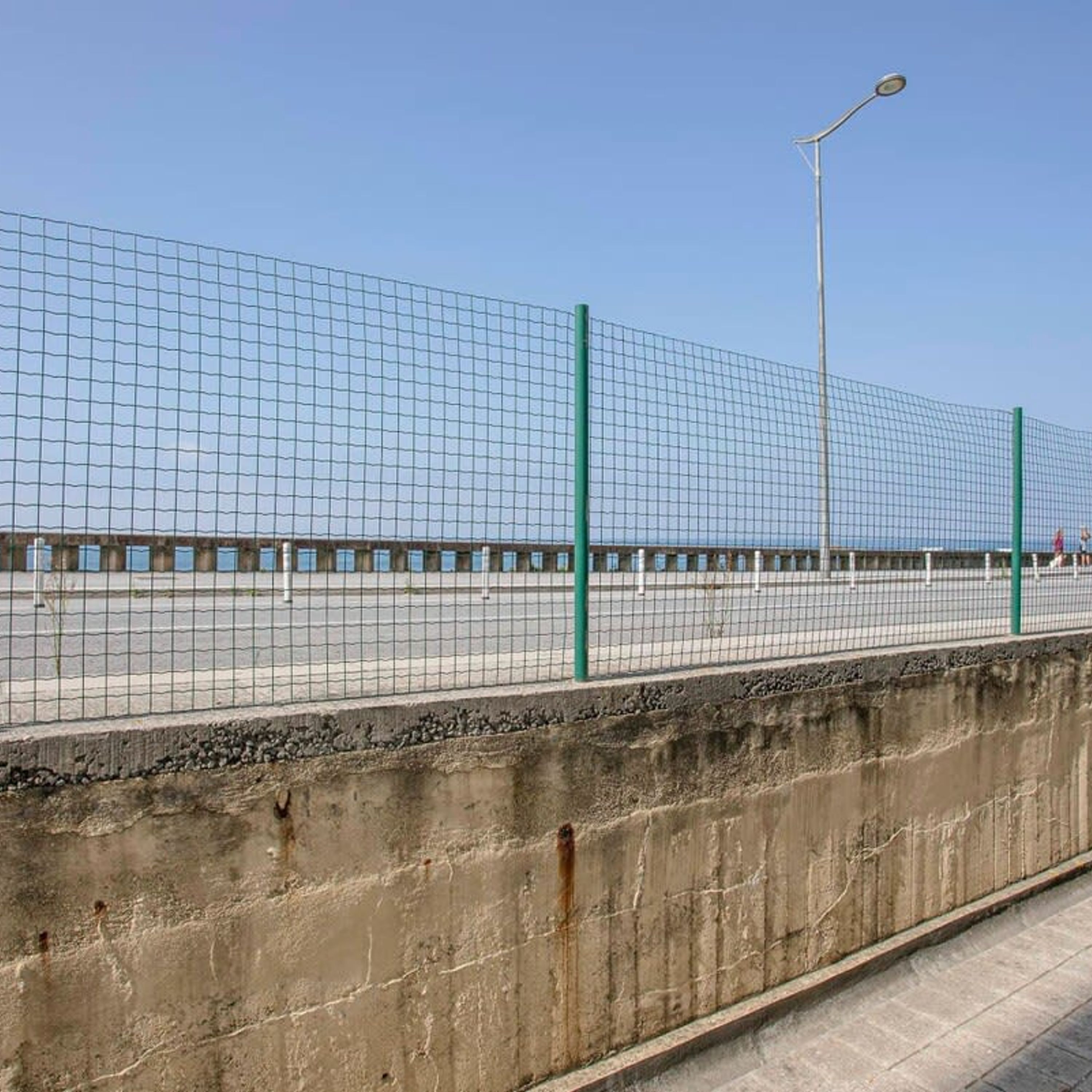 A concrete barrier with a metal fence and a street lamp.