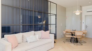 A modern living room with a sofa, a dining table with chairs, and large windows. - Liiiving in Porto - Modern Coastline Apartment (Porto)