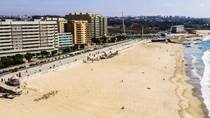 A wide sandy beach with a cityscape in the background, including high-rise buildings and a clear sky. - Liiiving in Matosinhos - High Sea Condo (Matosinhos)