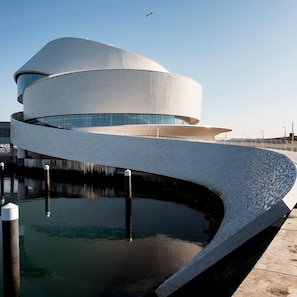 A modern architectural building with a unique curved design, situated by a body of water. - Liiiving in Matosinhos - High Sea Condo (Matosinhos)