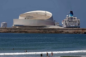 A modern building with a unique curved roof, a large water body in the foreground, and a cruise ship docked nearby. - Liiiving in Matosinhos - High Sea Condo (Matosinhos)
