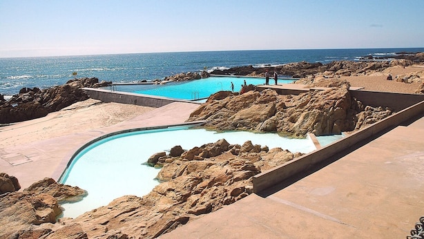 A pool area with a view of the ocean, surrounded by rocky terrain. - Liiiving in Matosinhos - High Sea Condo (Matosinhos)