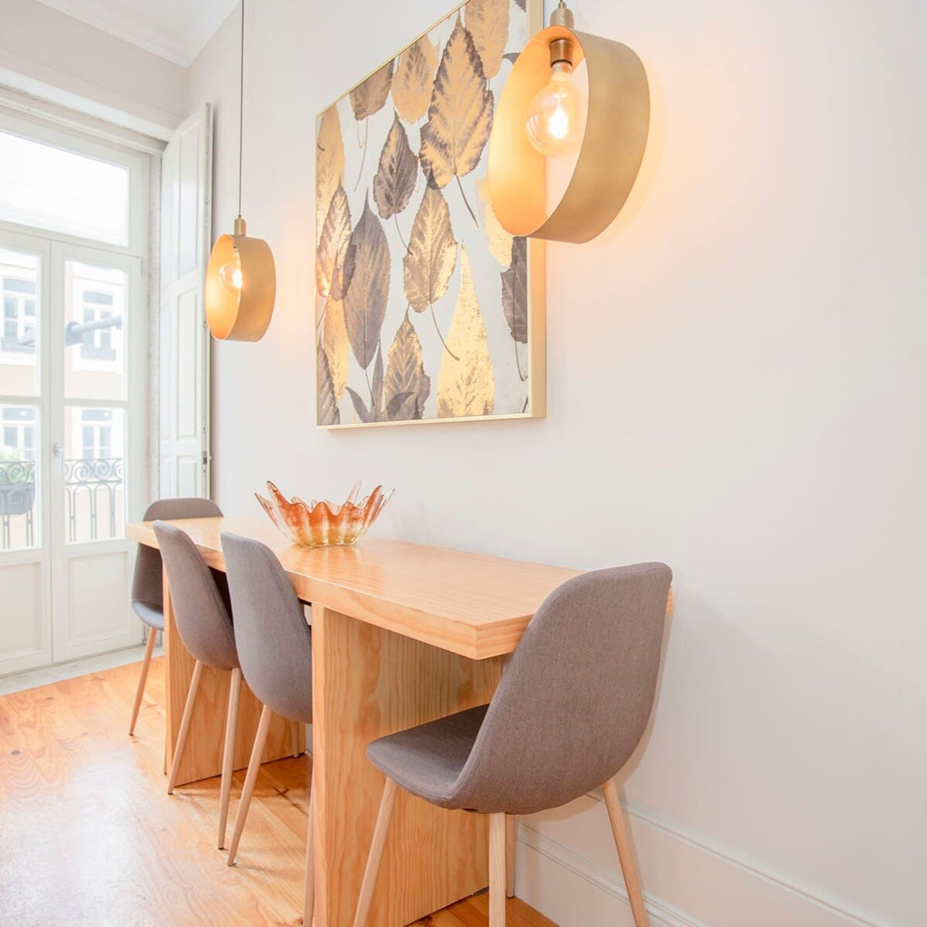 Ein Essbereich mit einem Holztisch, vier grauen Stühlen und einem Wandbehang mit Blätermotiv.