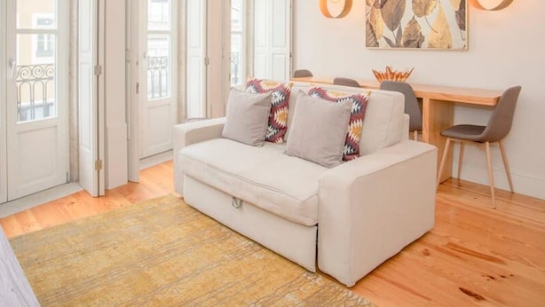 A modern living room with a white sofa, a dining table, and two pendant lights. - Liiiving in Porto - Ribeira Secret Apartment (Porto)