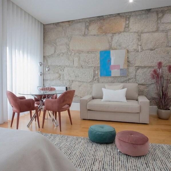 A modern living room with a stone wall, a glass table with chairs, a sofa, and a painting.