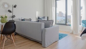 A modern living room with a grey sofa, a dining table with chairs, a TV, and a large window with curtains. - Liiiving in Porto Bright Light Studio (Porto)