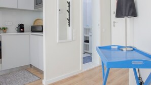 A modern kitchen with white cabinets, a microwave, and a coffee machine. There is a blue table with a lamp next to it. - Liiiving in Porto Bright Light Studio (Porto)