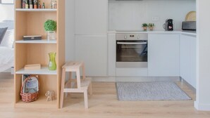 A modern kitchen with white cabinets, a built-in oven, and a microwave. There is a small wooden stool and a basket on the floor. - Liiiving in Porto Bright Light Studio (Porto)