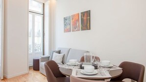 A modern dining area with a round table set for four, a grey sofa, and a window with a view. - Liiiving in Porto-mouzinho Residence Apartment 1F (Porto)