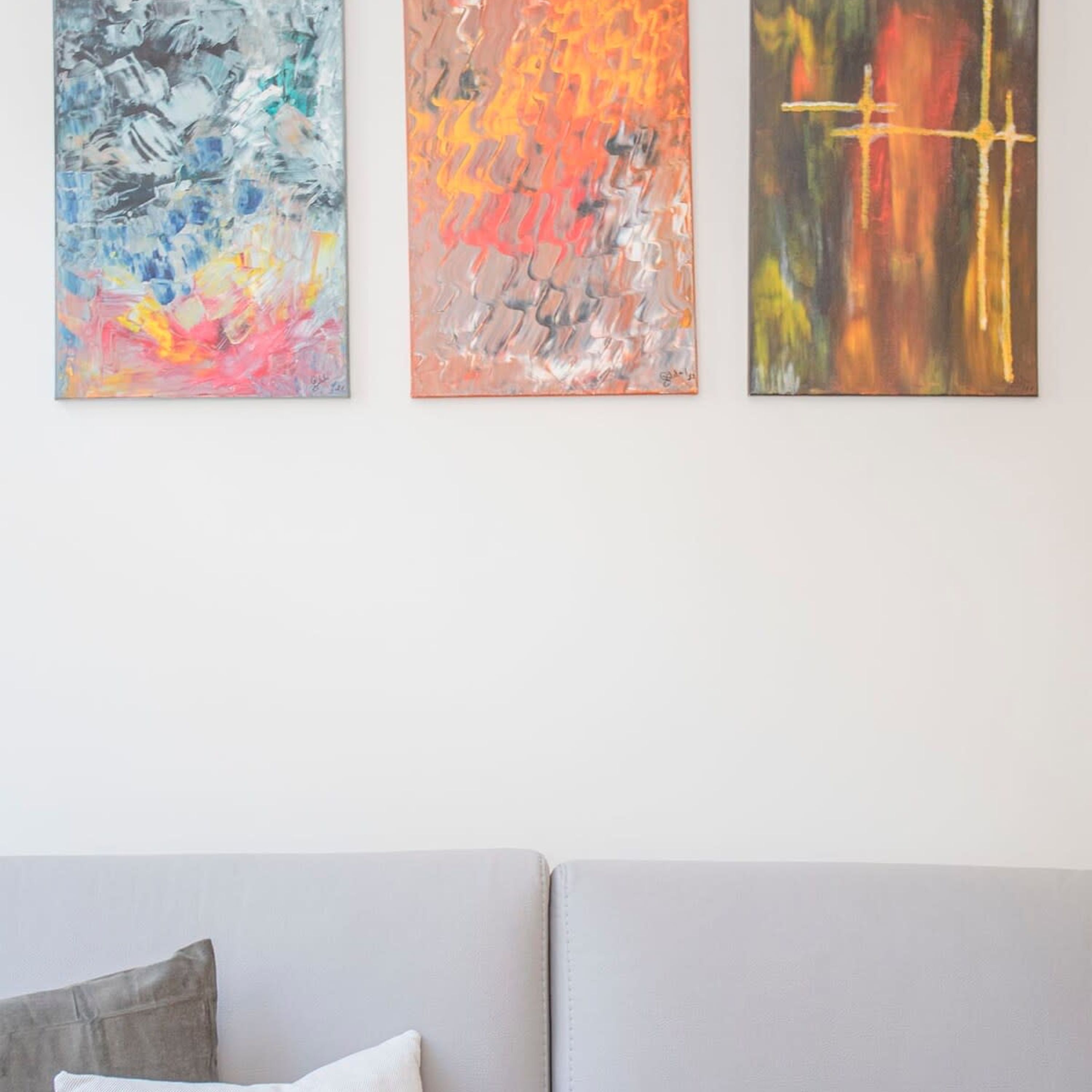 Drei abstrakte Gemälde an einer Wand über einem Sofa.