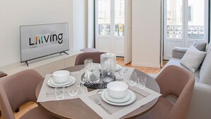 A dining area with a round table set for four, a flat-screen TV on the wall, and large windows with a city view. - Liiiving in Porto-mouzinho Residence Apartment 1F (Porto)