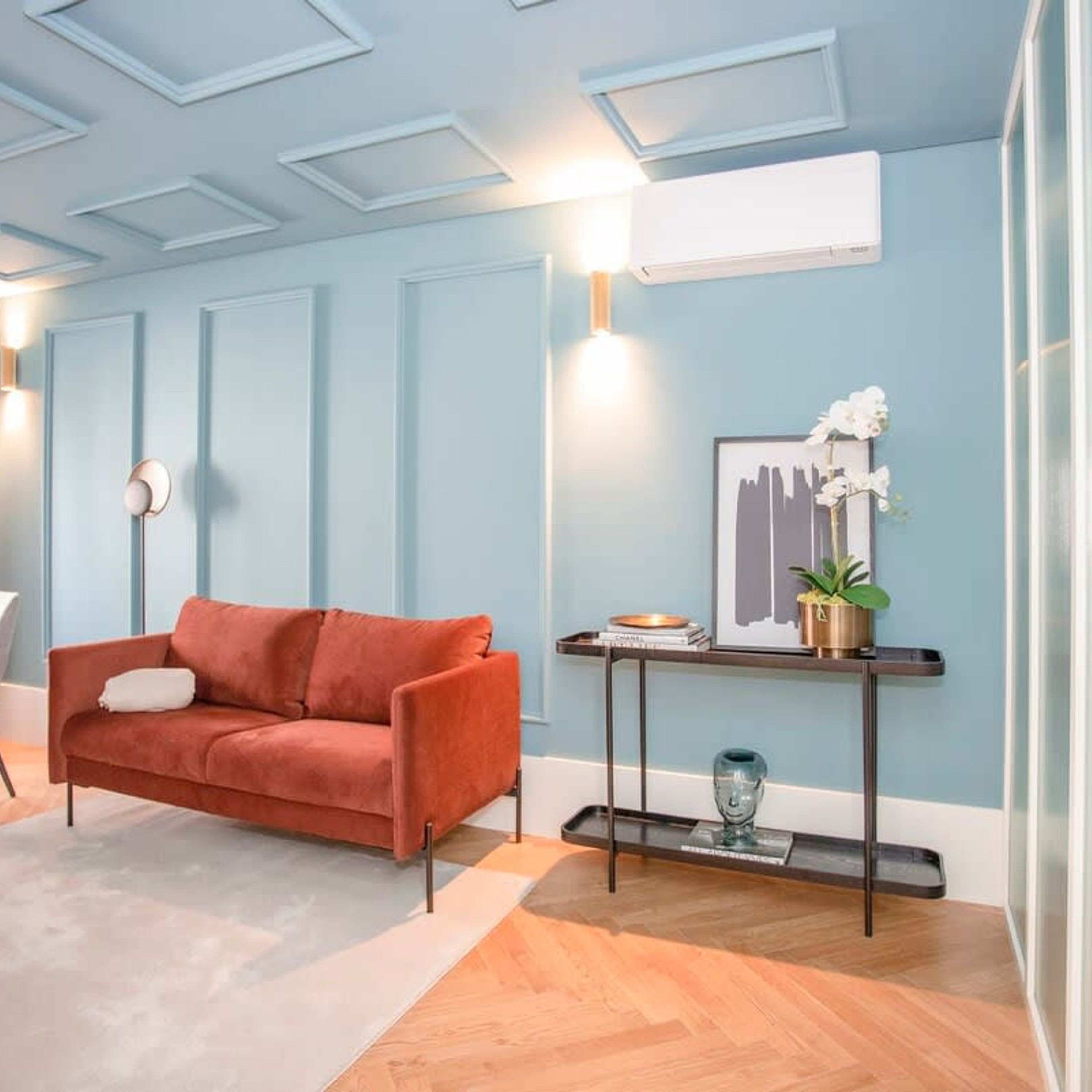 Ein Wohnzimmer mit einem roten Sofa, einem Couchtisch mit Büchern und einer Pflanze sowie einer Wand-Klimaanlage.