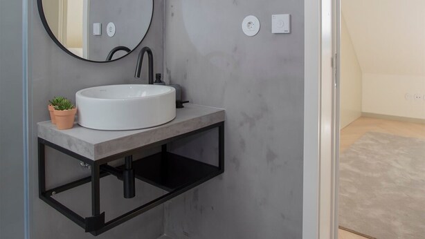 Un baño moderno con un lavamanos blanco, un grifo negro y un espejo redondo.