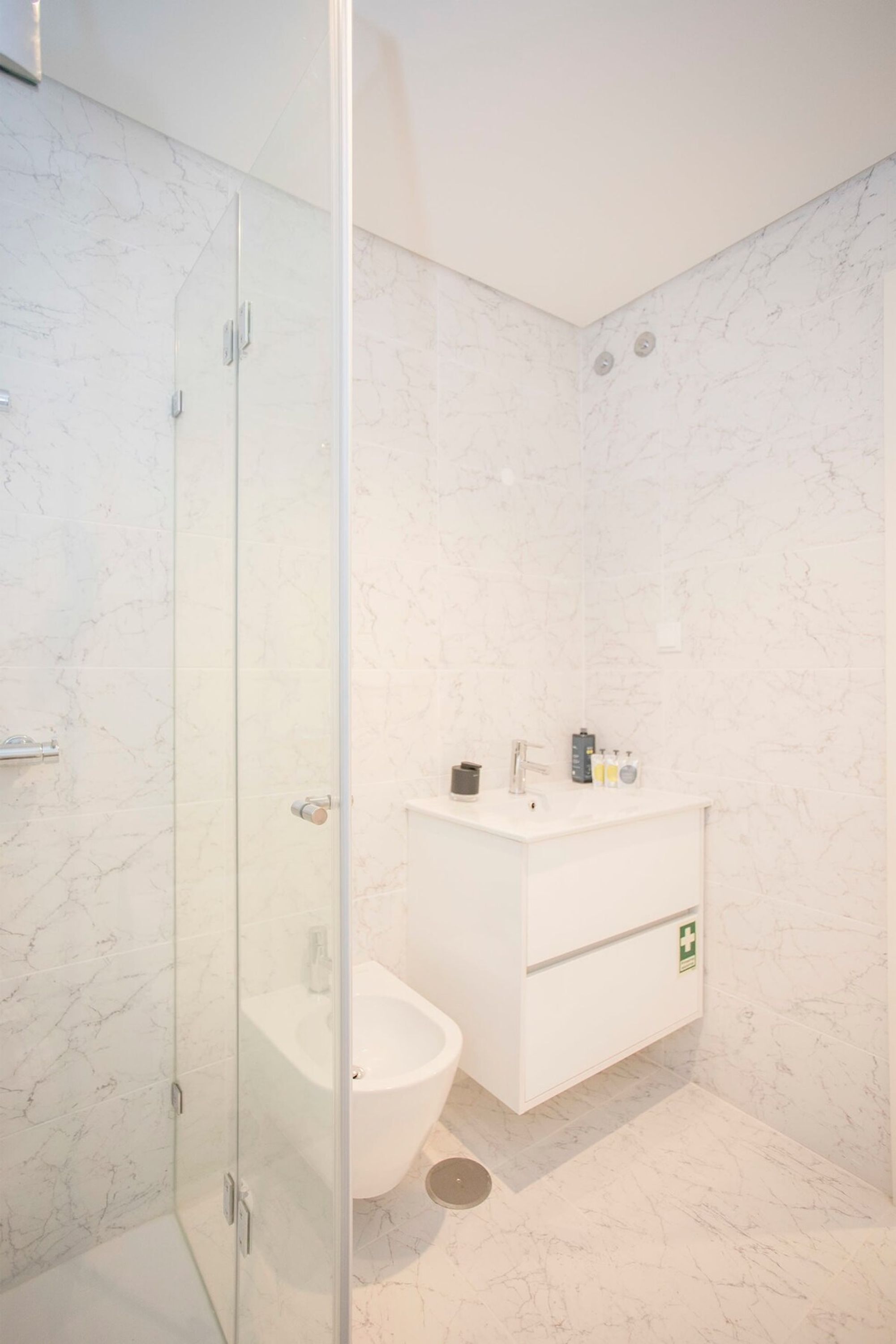 A modern bathroom with a glass-enclosed shower, a white sink, and a marble-tiled floor.