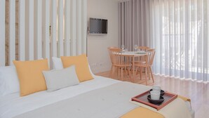A hotel room with a bed, a dining table with chairs, a TV mounted on the wall, and a window with curtains. - Liiiving in Porto Charming Downtown Delight I (Porto)