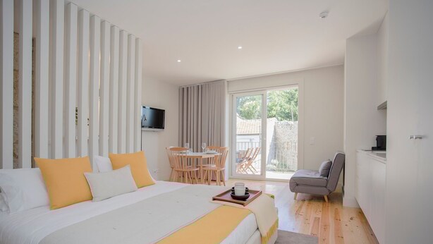 A modern hotel room with a large bed, a dining area, and a balcony. - Liiiving in Porto Charming Downtown Delight I (Porto)