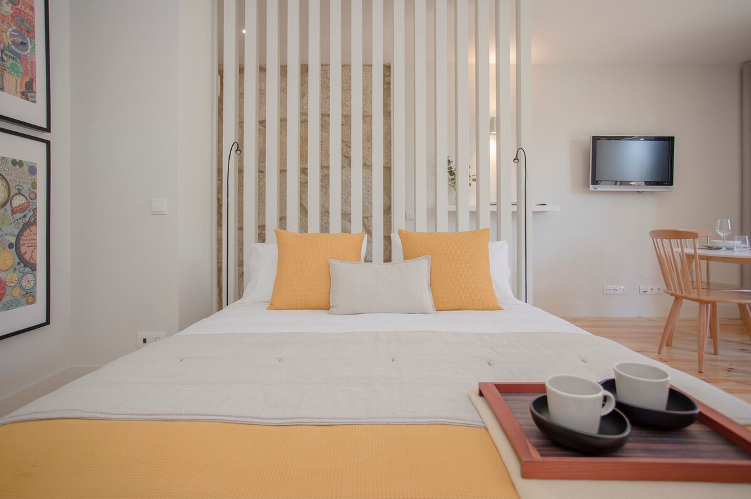 A hotel room with a bed, a TV, a dining area, and a tray with cups.