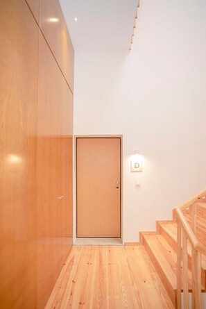 Eine Holztreppe führt zu einer Tür, über der eine Leuchte angebracht ist.