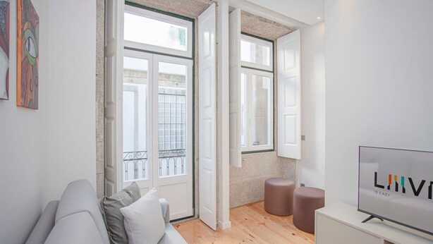 Una sala de estar moderna con un sofá gris, televisor y un balcón con barandillas de metal.