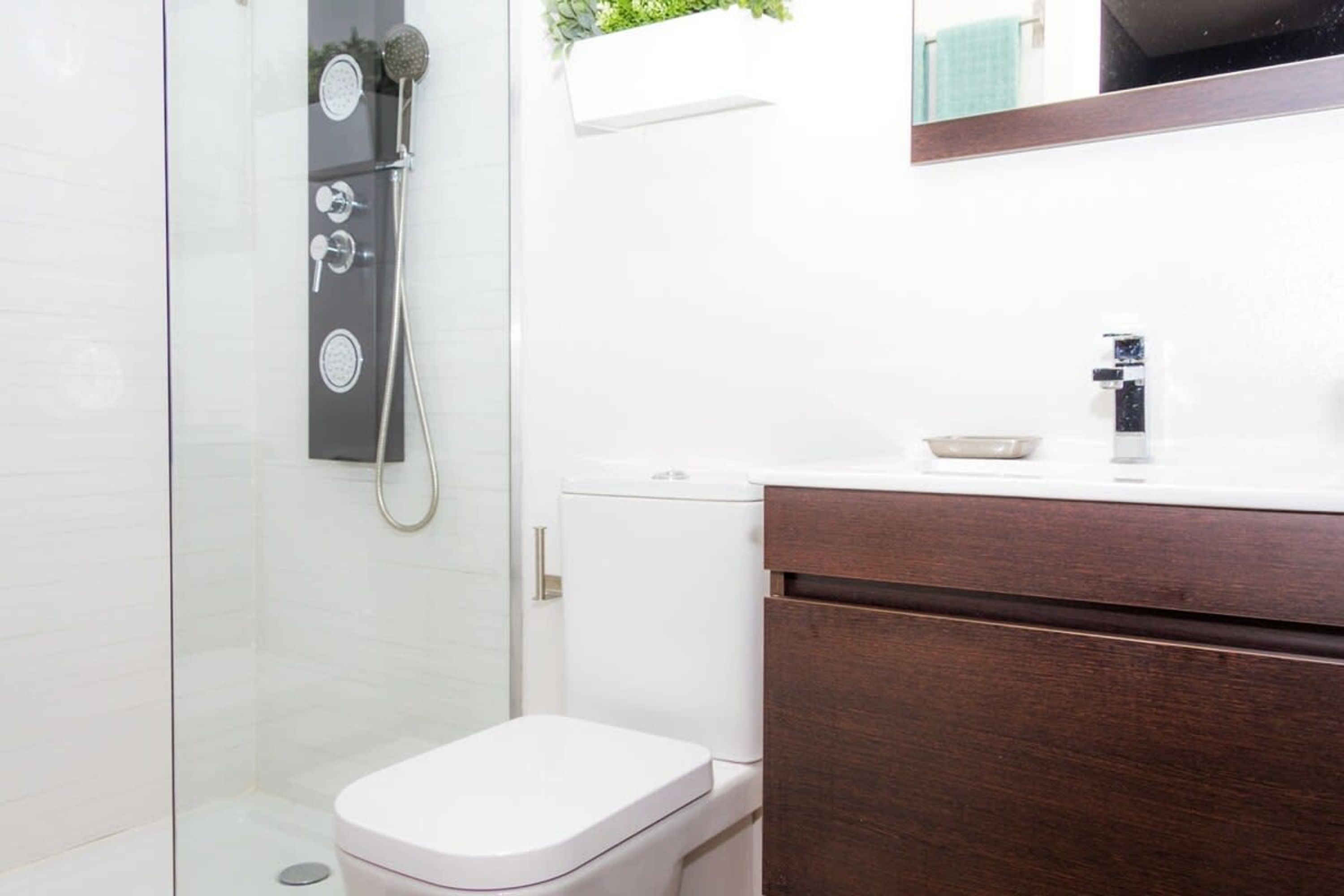 A modern bathroom with a glass shower enclosure, a white toilet, and a wooden vanity with a mirror.