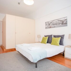 A bedroom with a bed, a wardrobe, a nightstand, a lamp, and a wall-mounted picture. - Liiiving in Porto Light Spacious Apartment (Porto)