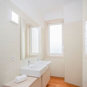 A small, bright bathroom with two sinks, a mirror, and a window. - Liiiving in Porto Light Spacious Apartment (Porto)