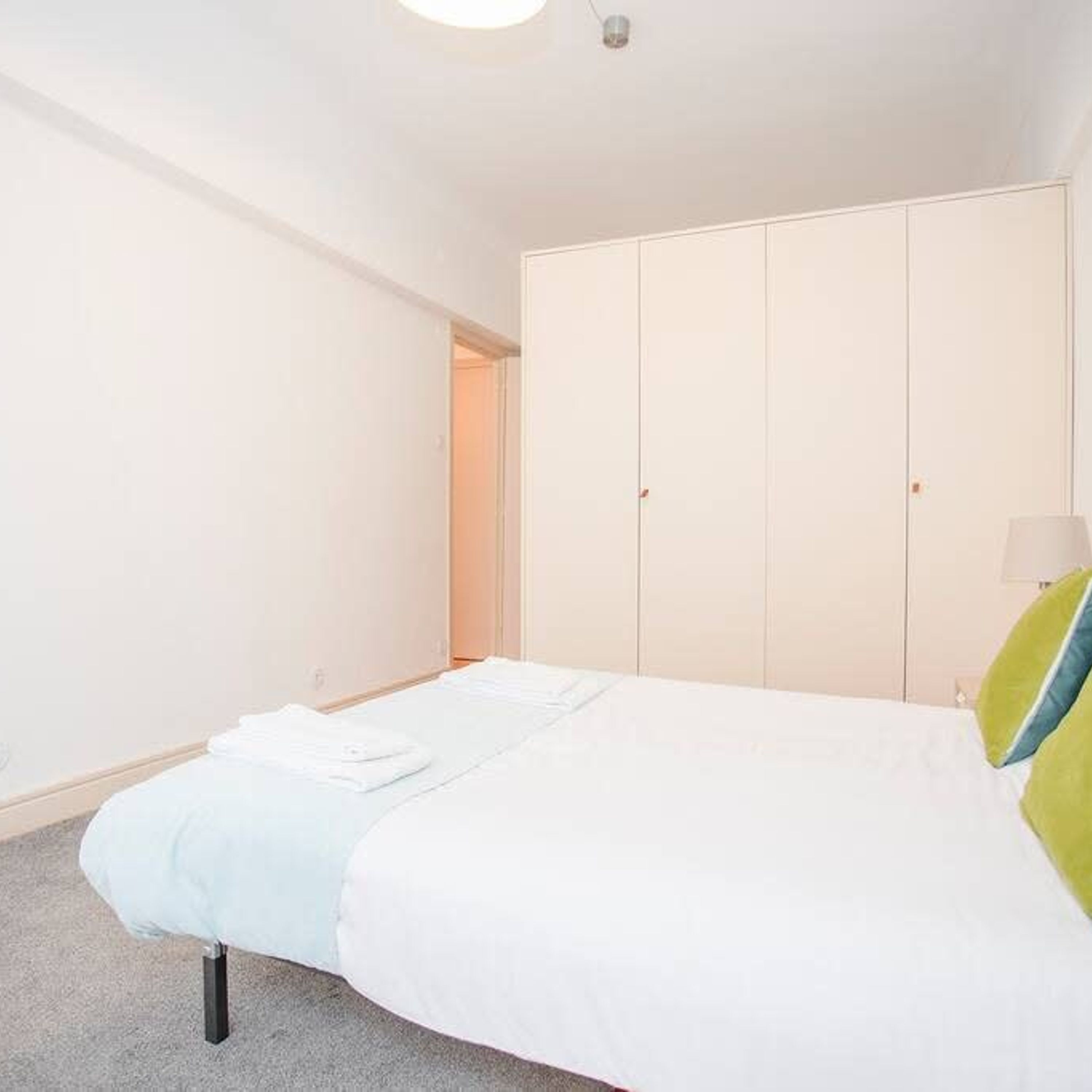 A bedroom with a bed, a wardrobe, and a door leading to another room.