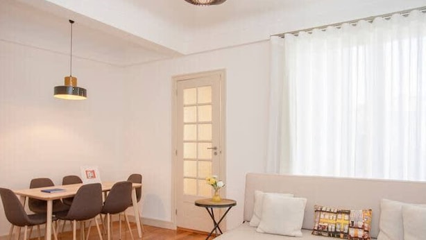 En moderne stue med en sofa, et spisebord med stole, en hængende lampe og en dør med et vindue.