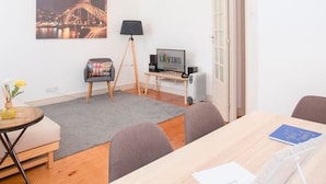 En moderne stue med stort vindue, spisebord, sofa, gulvlampe og fjernsyn.