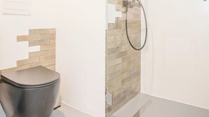 Egy modern fürőszoba üveg válaszfallal ellátott zuhanyzóval, WC-vel és csempézett fallal.