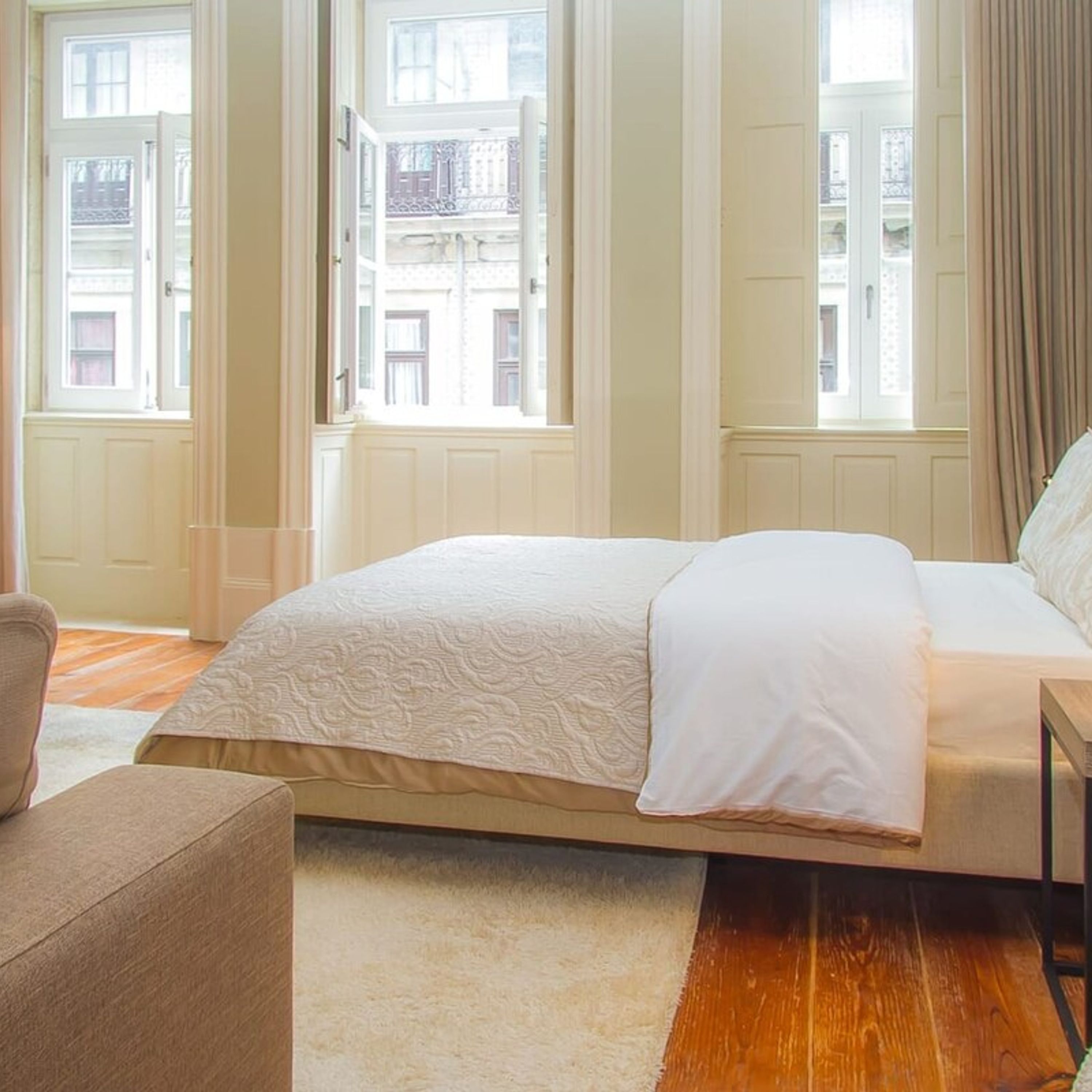 A bedroom with a bed, a chair, and large windows.