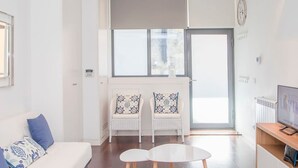 A modern living room with a white sofa, two white chairs, a small round table, and a TV on a wooden stand. - Liiiving in Porto - Carlos Alberto Apartment (Porto)