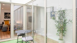 Um interior moderno com divisória de vidro, área de refeições com mesa e cadeiras, e um vaso de planta.