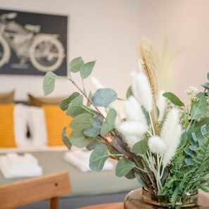 Une pièce comprenant une chaise en bois, un vase avec des feuilles vertes et des plantes blanches et duveteuses, et un mur orné d’une illustration de bicyclette.