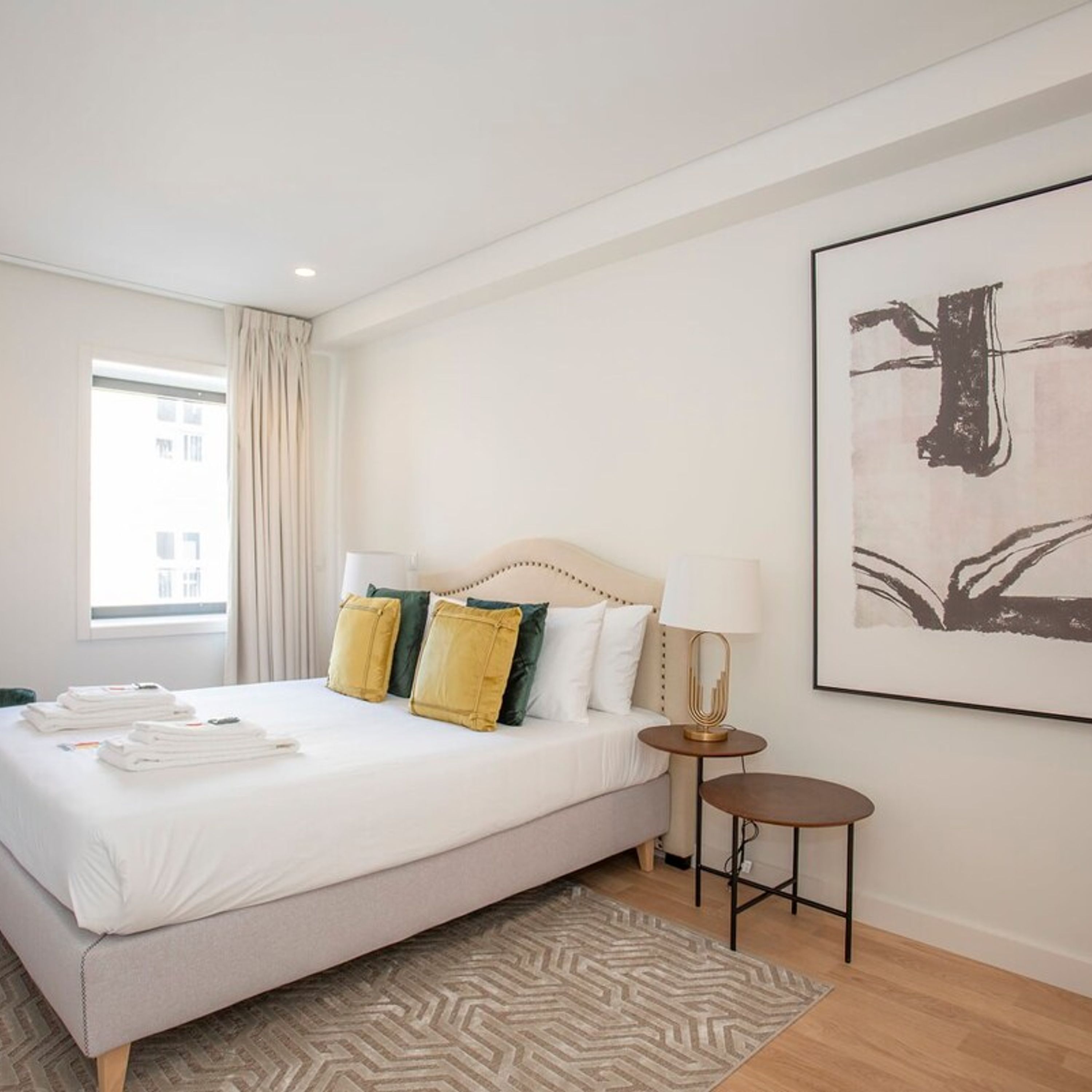 A hotel room with a large bed, a bedside table with a lamp, and a framed artwork on the wall.