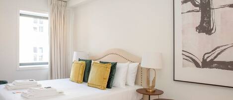 A hotel room with a large bed, a bedside table with a lamp, and a framed artwork on the wall.