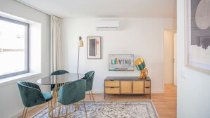 Un salon moderne avec une table ronde en verre, des fauteuils de couleur turquoise, un buffet en rotin et une œuvre d’art encadrée accrochée au mur.
