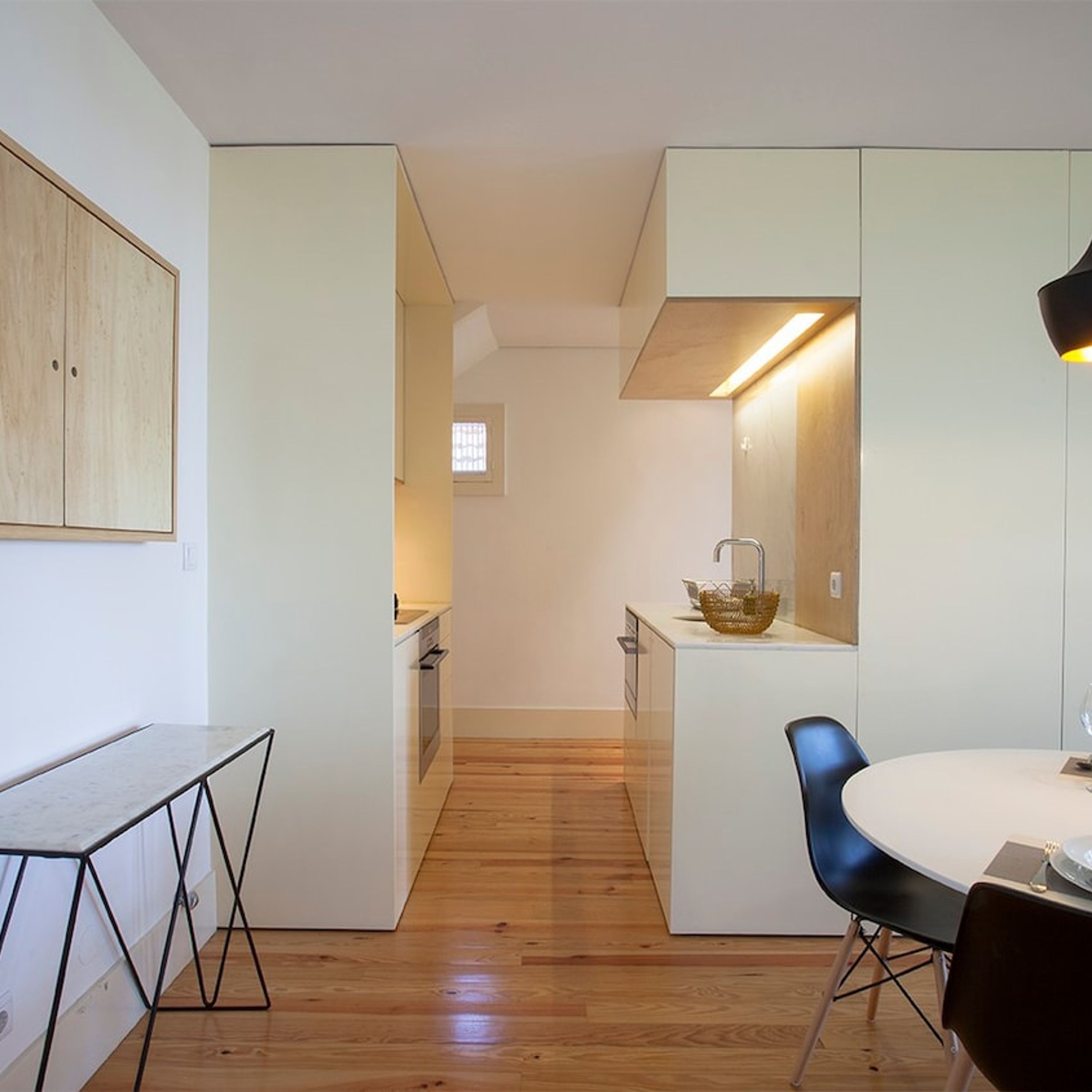 A compact kitchen with a dining area, wooden flooring, and a modern light fixture.