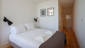 A neatly made bed with white linens and a brown blanket, a black wall lamp, and two framed pictures on the wall. - Liiiving in Porto Central Secret Balcony (Porto)