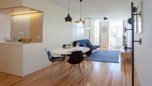 A modern kitchen with white cabinets, a dining area with a round table and black chairs, and a blue sofa. - Liiiving in Porto Central Secret Balcony (Porto)