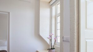 A corner room with a window, a small plant on a counter, and a dark rug on the floor. - Liiiving in Porto Central Secret Balcony (Porto)