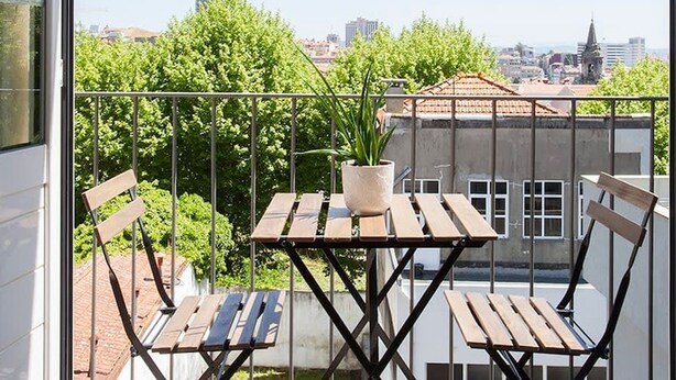 A balcony with a table and chairs, a potted plant, and a cityscape view. - Liiiving in Porto Central Secret Balcony (Porto)