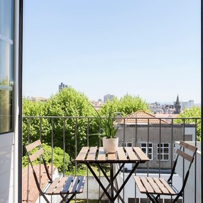 A balcony with a table and chairs, a potted plant, and a cityscape view. - Liiiving in Porto Central Secret Balcony (Porto)