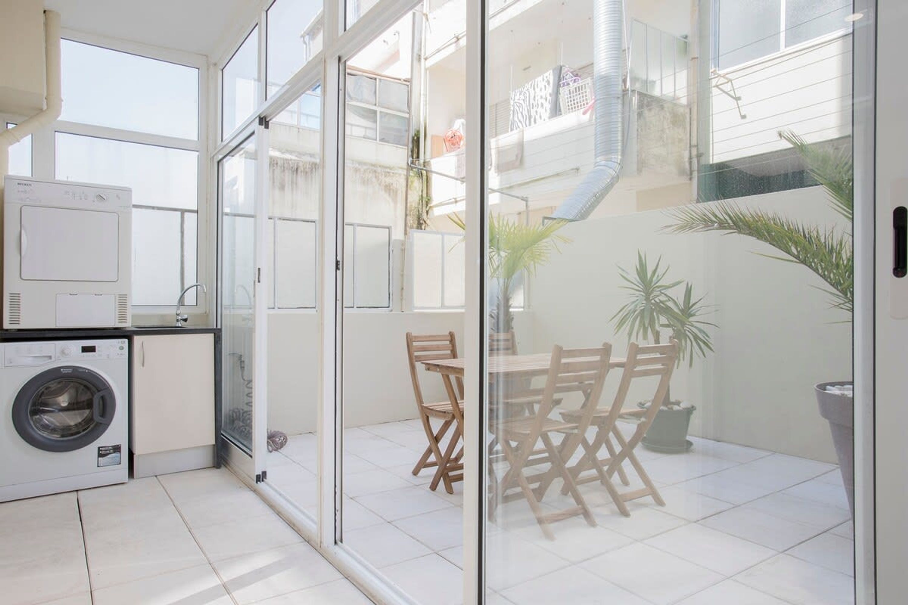 A laundry area with a washing machine and dryer, a glass door leading to a balcony with chairs and potted plants.