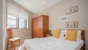A hotel room with a large bed, a wooden wardrobe, a chair, and a window with blinds. - Liiiving in Porto Terrace Downtown Apartment (Porto)