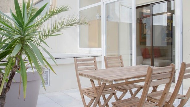 An outdoor patio with a wooden table and chairs, a large potted plant, and a glass door leading to an interior space. - Liiiving in Porto Terrace Downtown Apartment (Porto)