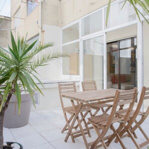 An outdoor patio with a wooden table and chairs, a large potted plant, and a glass door leading to an interior space. - Liiiving in Porto Terrace Downtown Apartment (Porto)