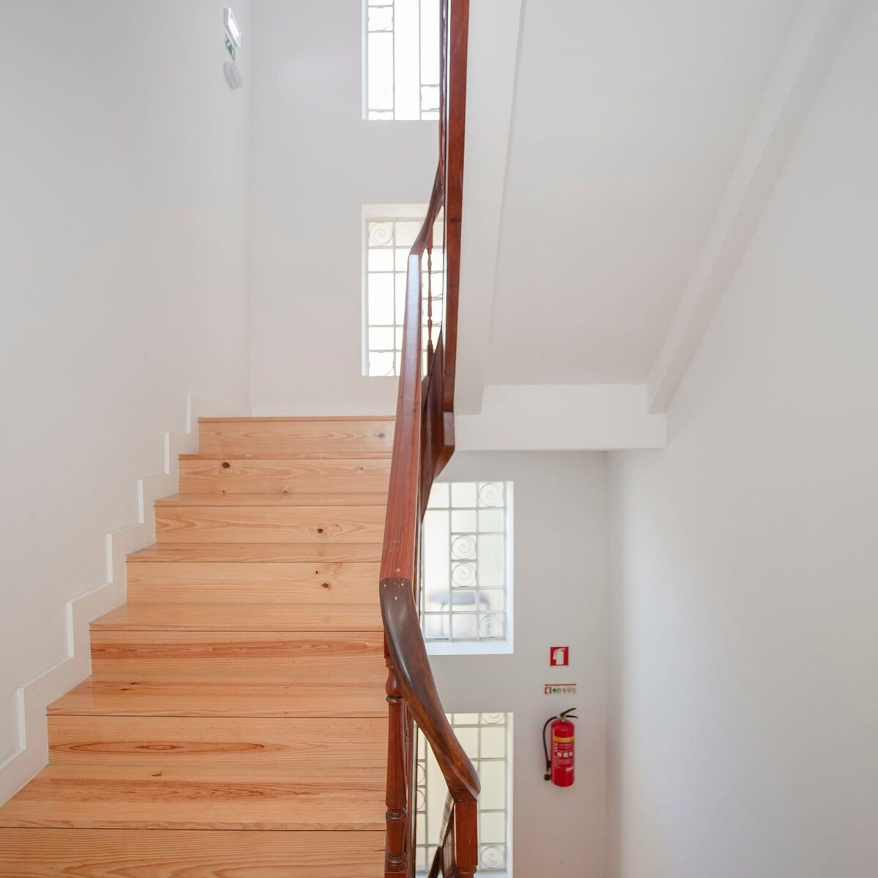 A wooden staircase with a handrail, white walls, and a fire extinguisher mounted on the wall.